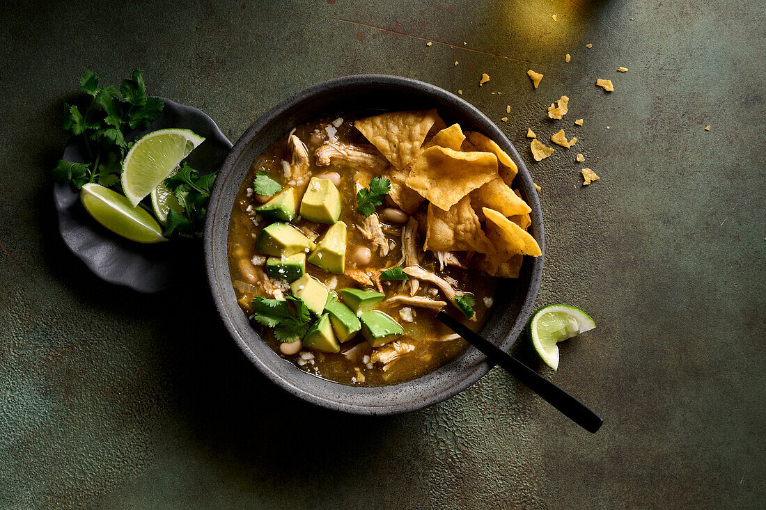 Green chicken and chilli soup in a bowl, garnished with avocado, coriander, tortillas and cotija cheese