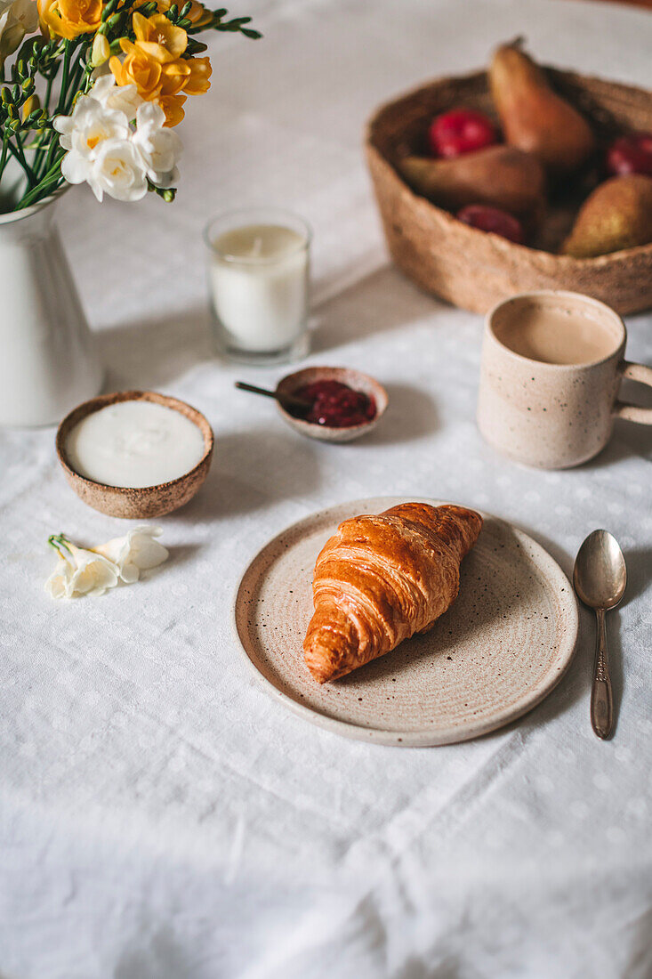 Frühstücksszene mit Croissant, Kaffee, Joghurt und Obst