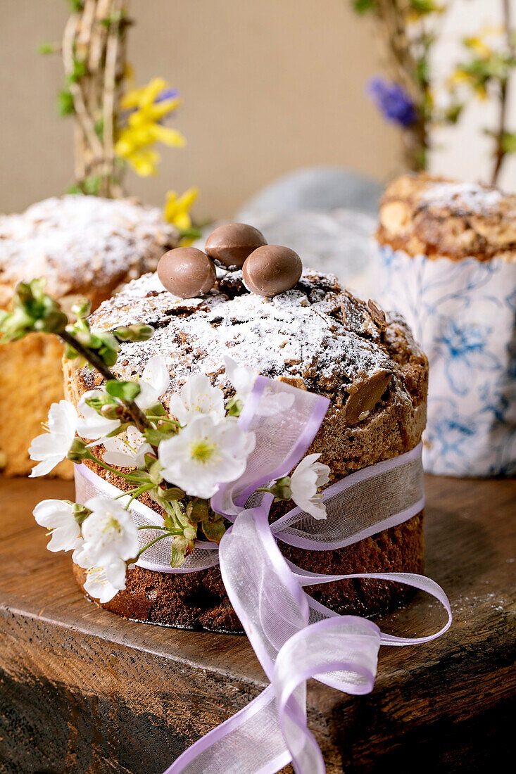 Homemade Italian traditional Easter panettone cake, decorated by chocolate eggs, pink ribbon and blossoming cherry tree flowers standing on wooden table. Traditional Easter European bake. Close up