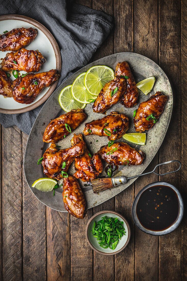 Glazed chicken wings on metal plate and serving platter with lime, sauce and spring onions