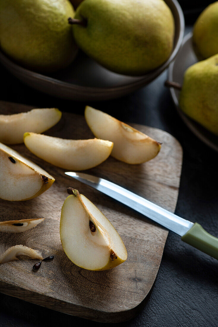 There is a pear cut in half, slices and a knife on a cutting board. Fruits on a plate.