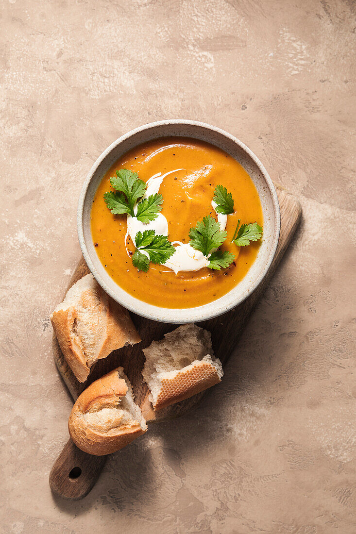 Butternut squash soup and baguette on wooden board.