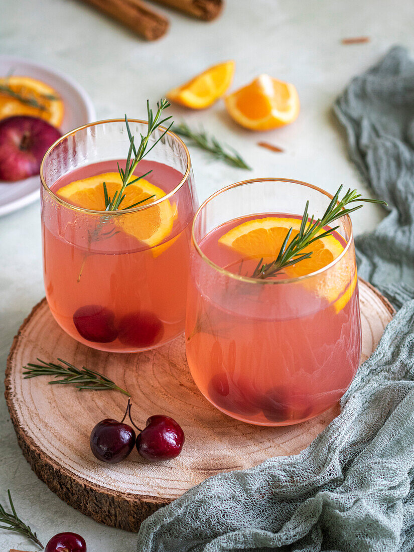 Christmas punch in glasses, decorated with fresh cherries, orange and rosemary