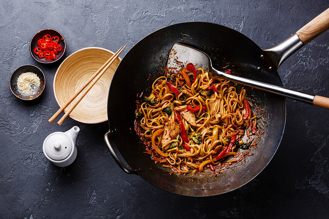 Udon noodles with chicken and vegetables in a wok pan on a dark stone background