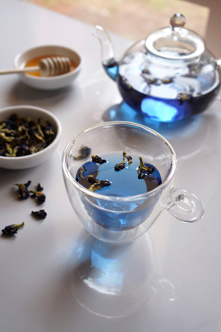 Blauer Schmetterlingsblütentee mit gläserner Teekanne und Tasse in Großaufnahme