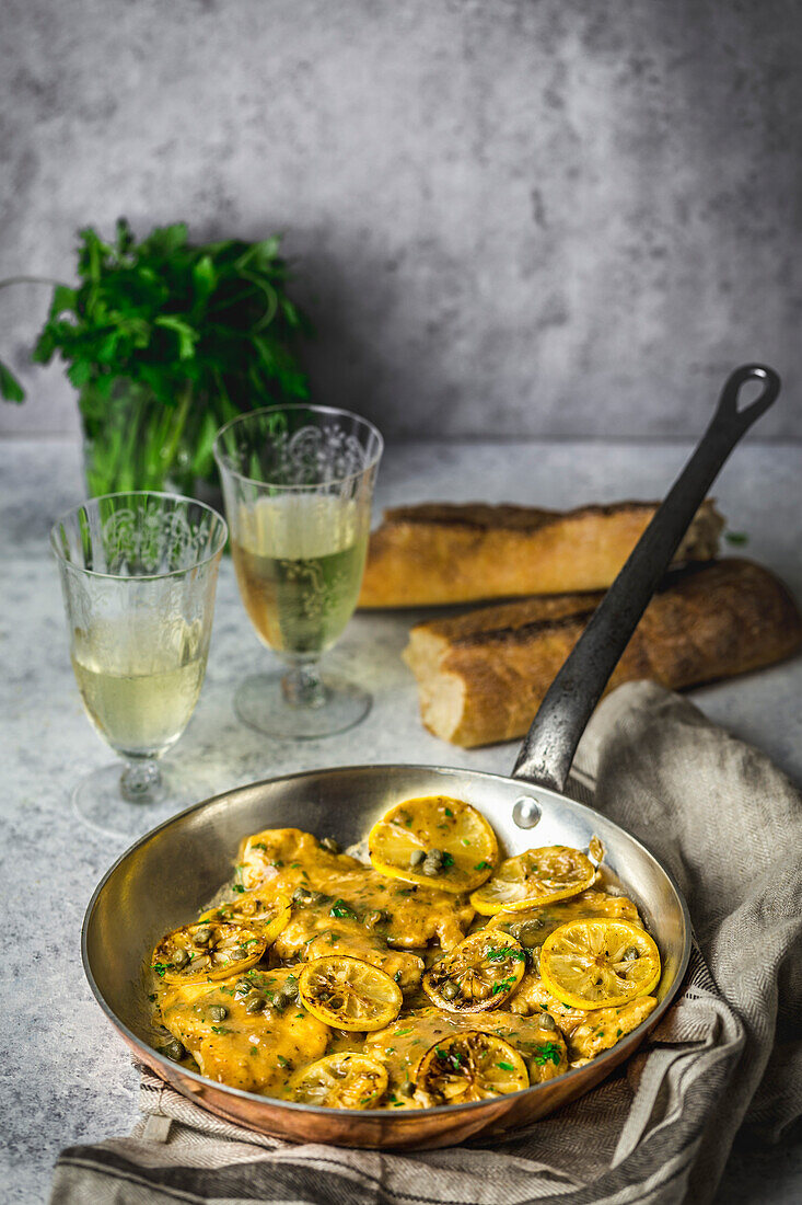 Hähnchen, Zitronenscheiben und Kapern in einer Kupferpfanne, mit Petersilie, Brot und Weißwein