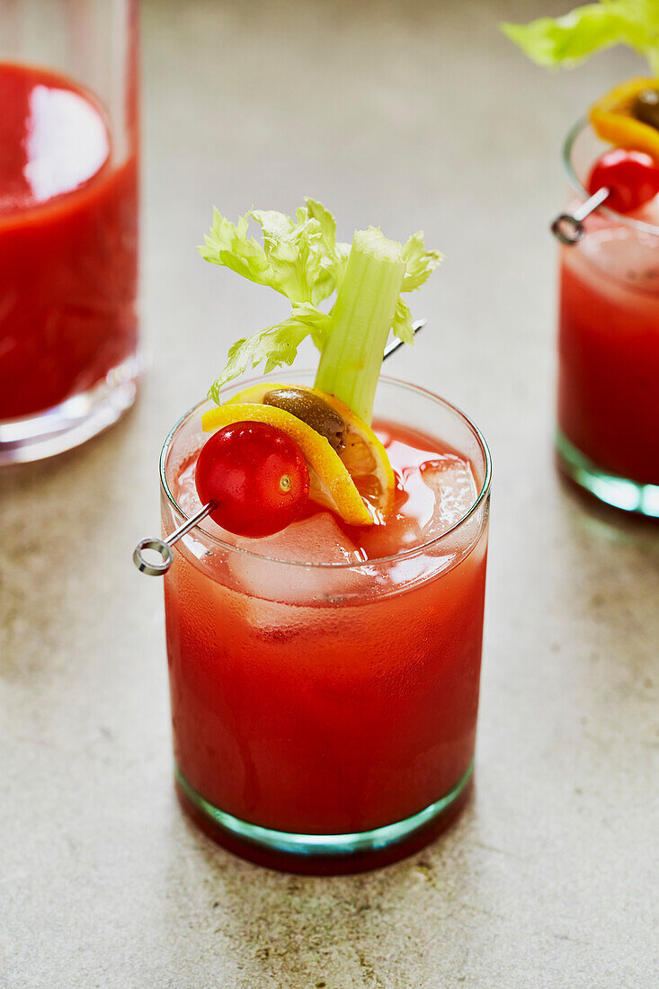 Bloody Mary cocktail with celery, tomato and olive garnish on a sage-green background