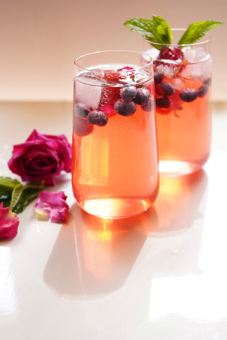 Beeren- und Rosenblütenschorle erfrischendes Sommergetränk auf weißem Tisch. Nahaufnahme von zwei Gläsern mit Leerzeichen