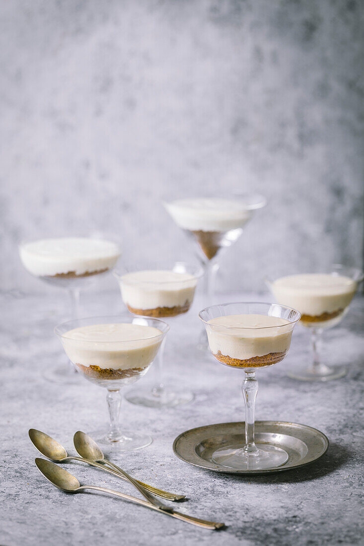 Arrangement of vanilla parfaits with biscuit crumbs in vintage cocktail glasses on grey background and small silver plate