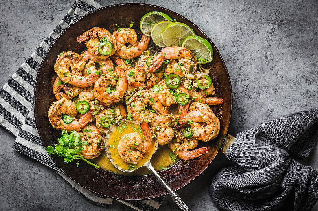 Garnele mit Chili, Limette und Koriander in Buttersauce, Stahlpfanne mit grauen Leinenservietten und Silberlöffel