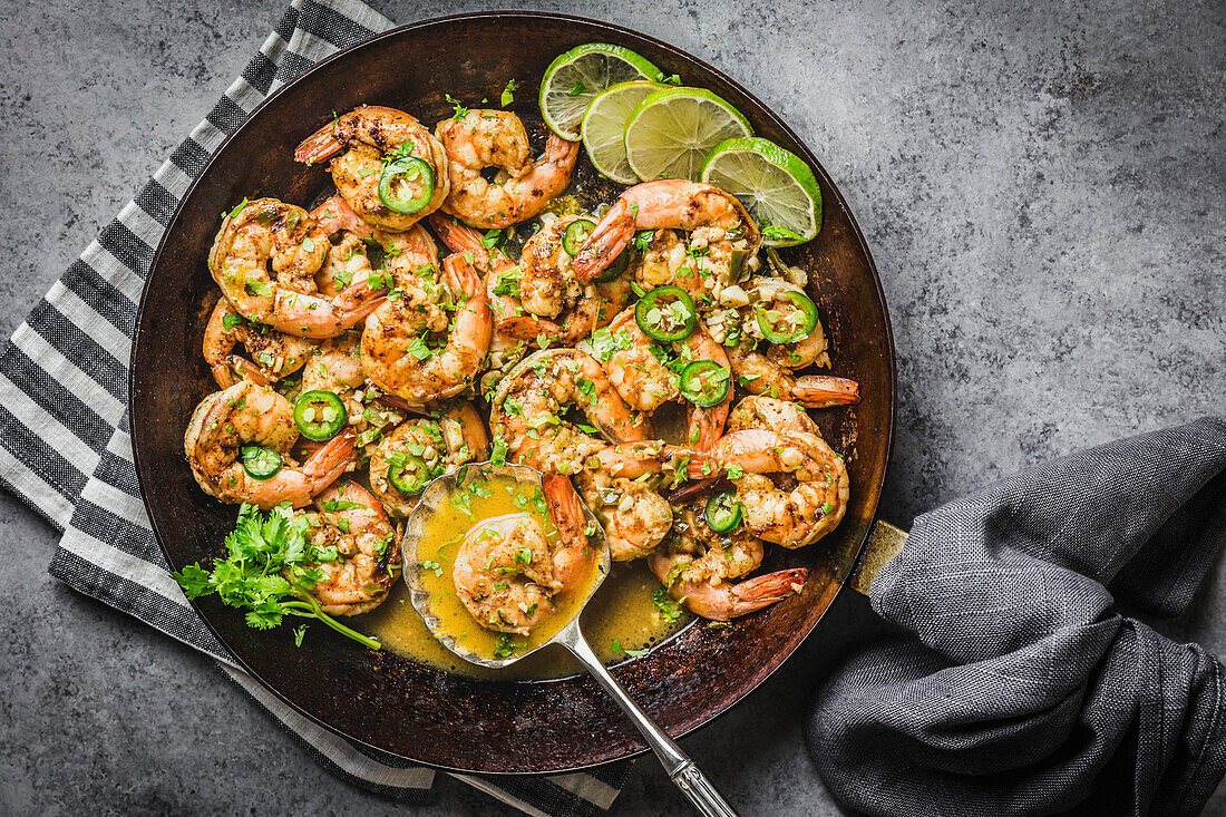 Shrimp with Chili, Lime and coriander in butter sauce, carbon steel skillet with gray linen napkins and silver spoon