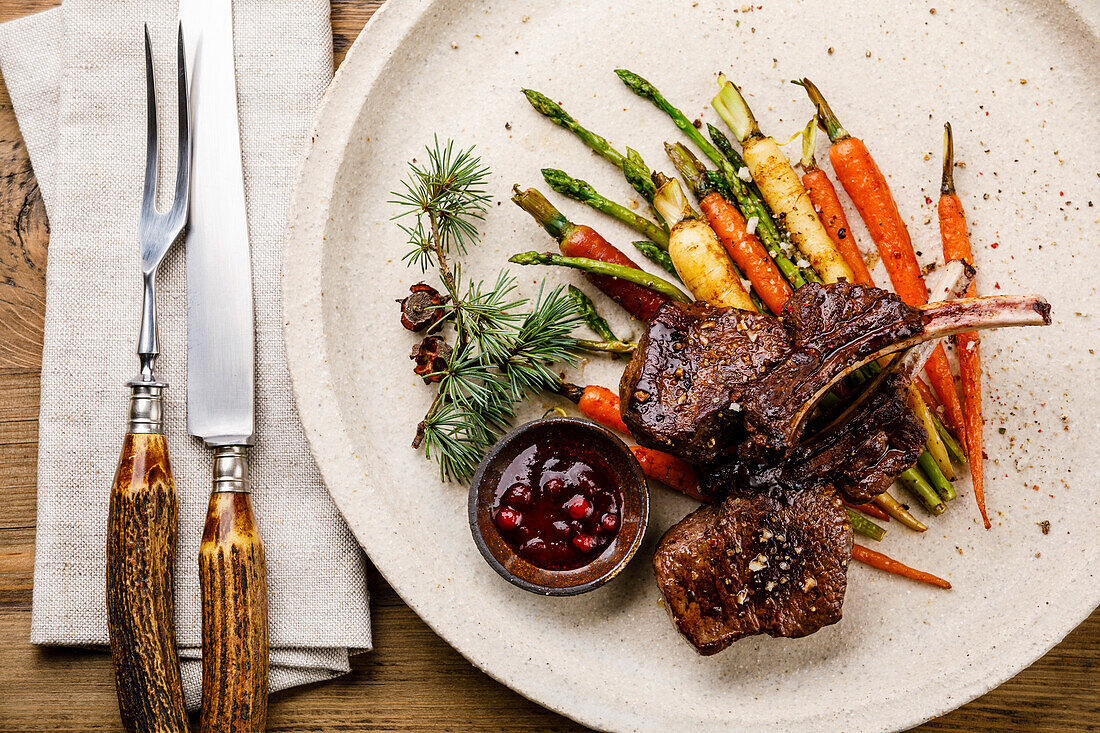 Grilled venison ribs with baked vegetables and berry sauce on a wooden base