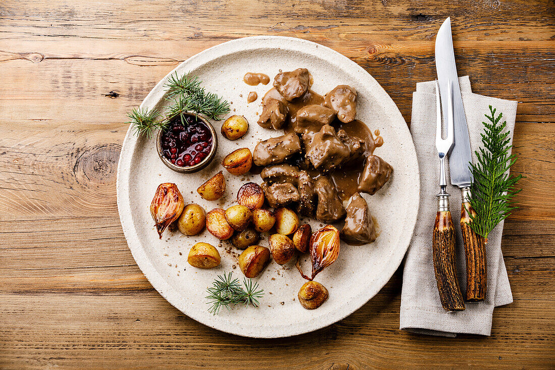 Braised venison in sauce with roast potatoes and berry sauce on a wooden table
