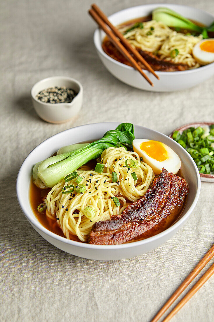 Ramen, Schweinebauch, Bok Choy und Ei vor einem hellen, neutralen Hintergrund