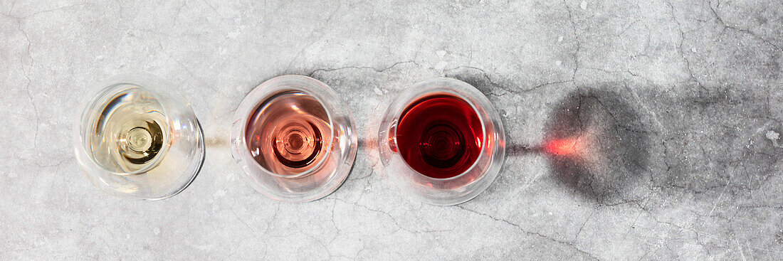 Red, rosé and white wine in glasses on a grey stone background. Wine bar, winery, wine tasting concept. Minimalistic trendy photography