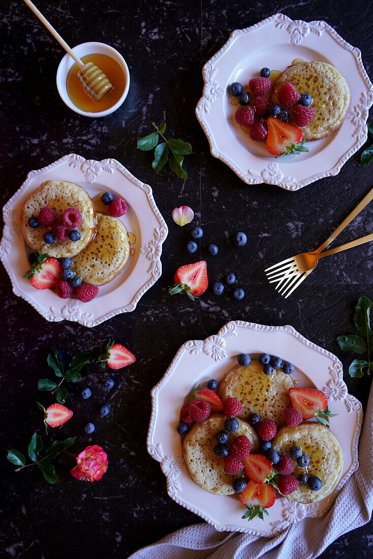 English style crumpets served with berries and honey on black marble background, flatlay.
