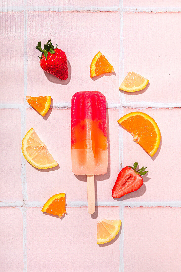 Fruit popsicle with ingredients on a pink tiled background