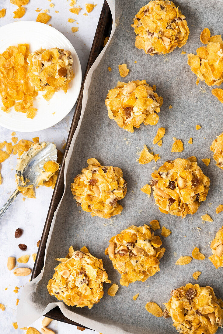 Balls of cookie dough rolled in cornflakes on a baking tray.