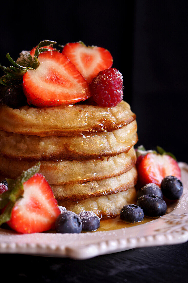 Stack of English style crumpets with berries and honey, closeup.