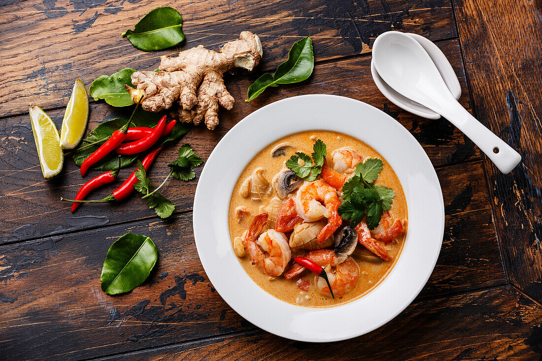 Tom Yam kung Scharfe thailändische Suppe mit Garnelen, Meeresfrüchten, Kokosmilch und Chilischoten in einer Schüssel auf Holzuntergrund