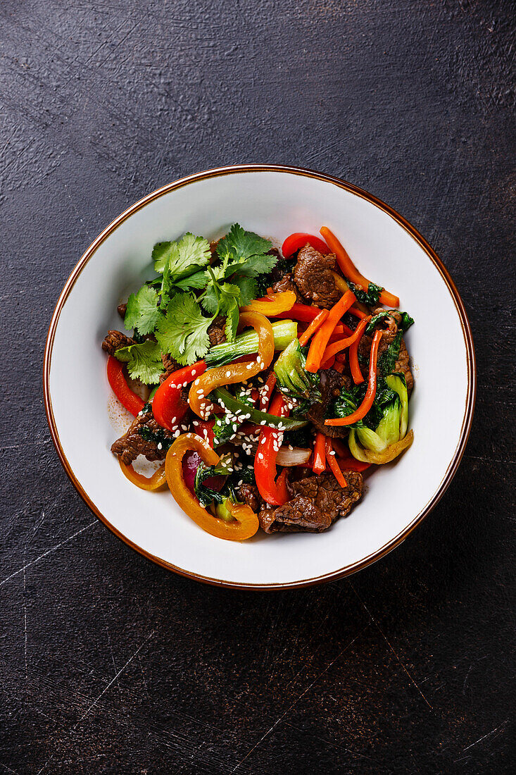 Roasted Szechuan beef with vegetables in a bowl on a dark background