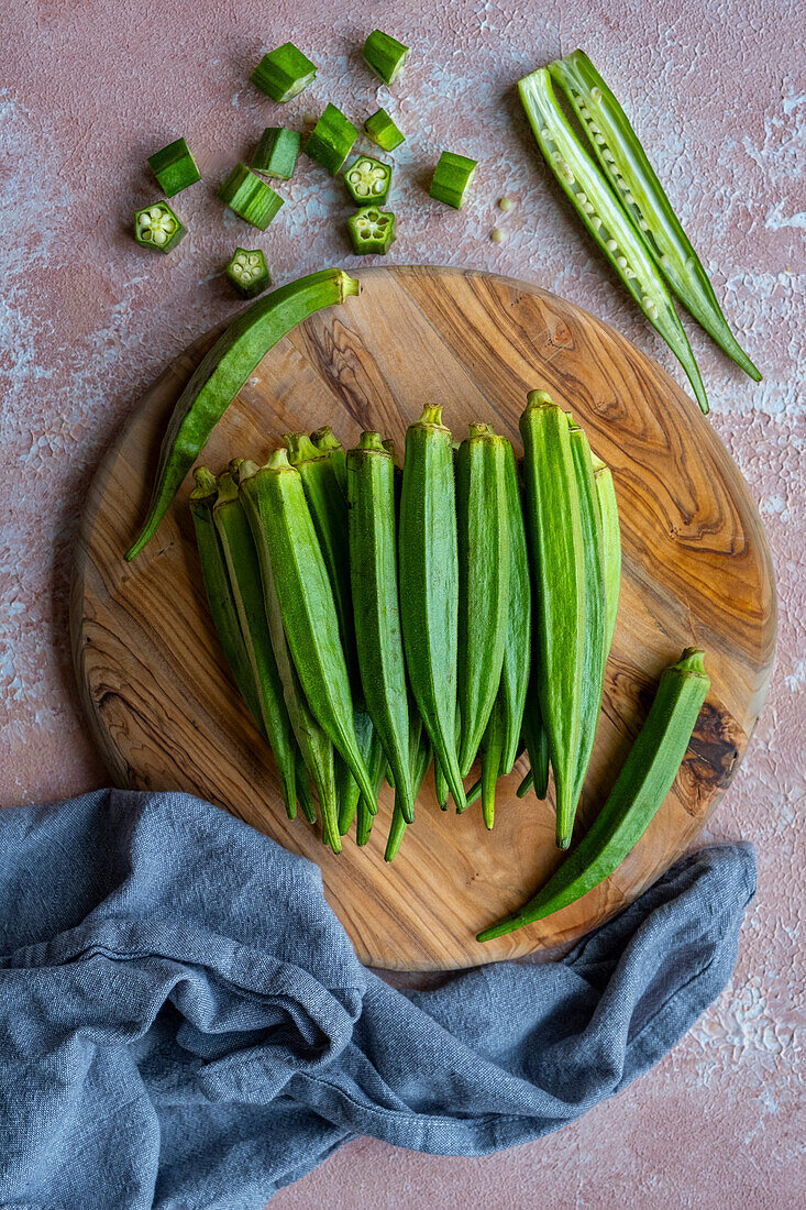 Fresh green okra pods on a round wooden cutting board.