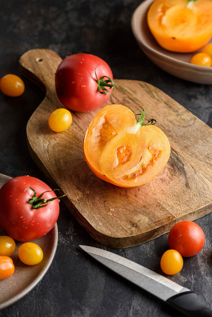 Half a tomato on a chopping board. Nearby are various yellow and red tomatoes