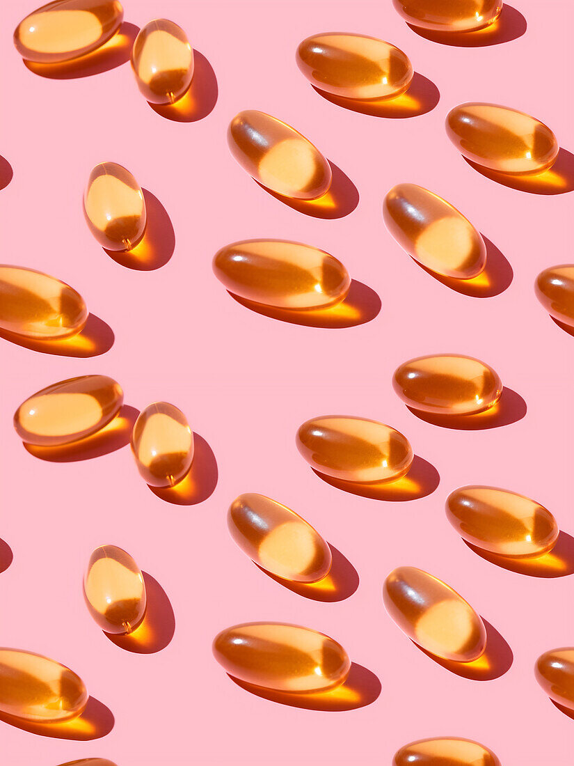 Top view composition of orange vitamin pills scattered on pink background in light studio