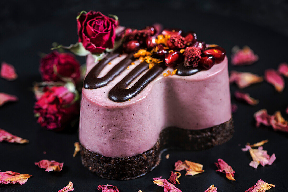 Herzkuchen, dekoriert mit Granatapfel und Erdbeeren. Dessert auf einem schwarzen Teller mit Rosen