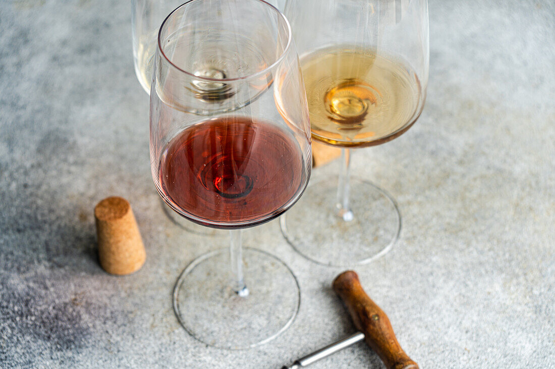 High angle of three main types of Georgian dry wines - white, red and amber - on a grey concrete table with a corkscrew and a cork