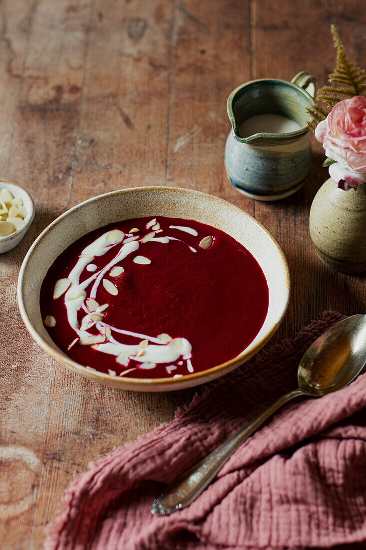 A bowl of beetroot soup with cream and almond flakes on a wooden table