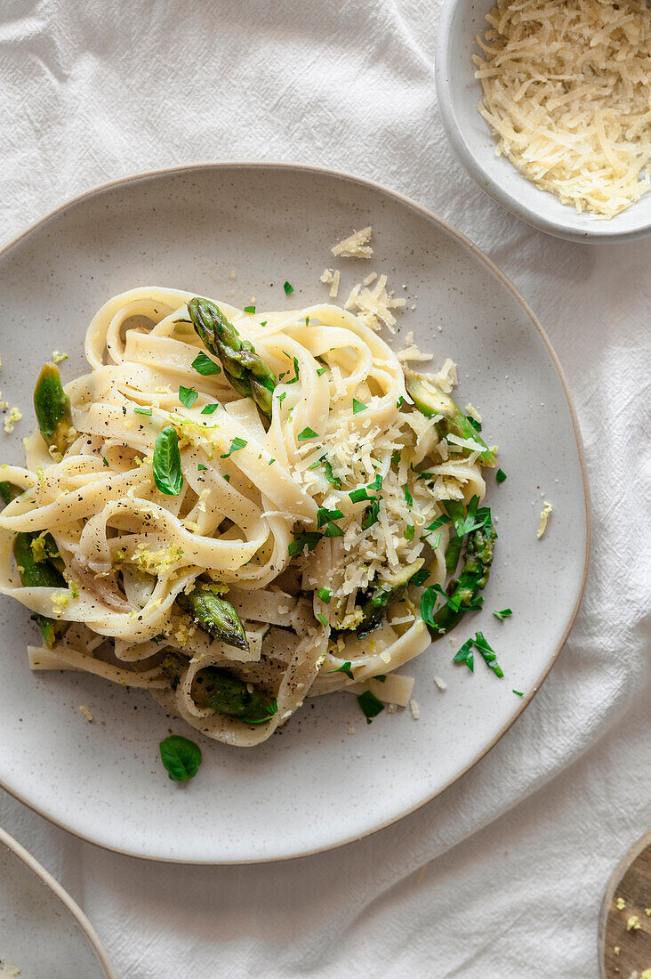 Zitronige Pasta mit Spargel, veganem Käse und frischem Basilikum auf einem frühlingshaften, luftigen Tisch