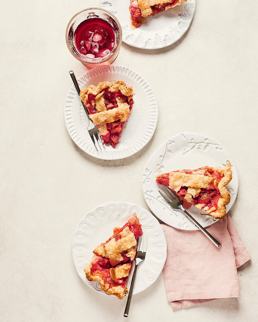 Vier Teller veganer Erdbeer-Rhabarber-Kuchen mit Hibiskus-Eisgetränk auf hellem Hintergrund