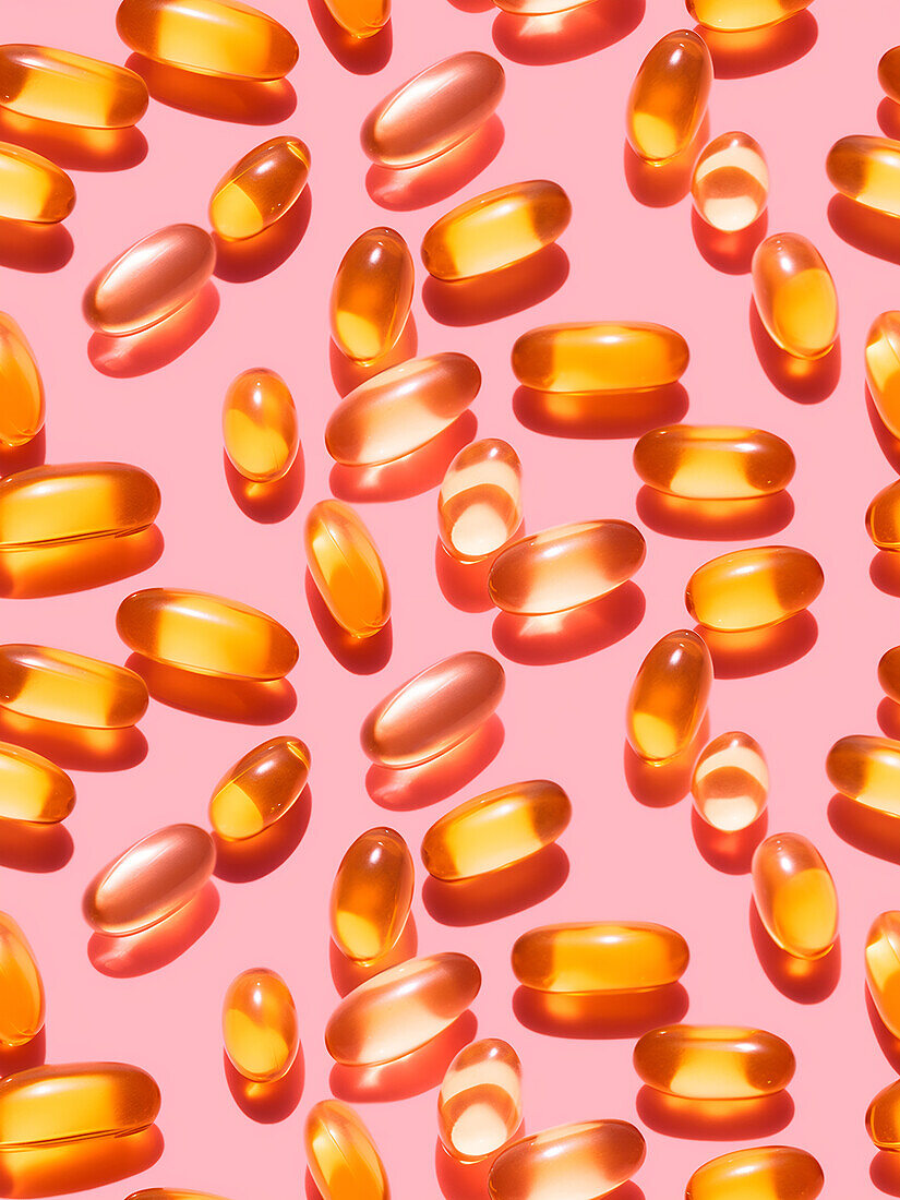 Composition of orange-coloured vitamin pills on a pink background in a bright studio viewed from above