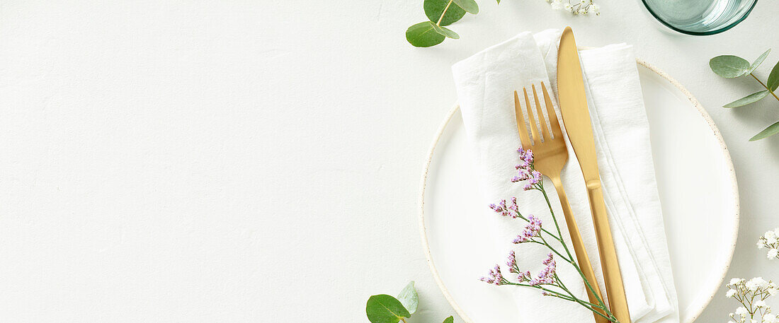 Gold Cutlery with eucalyptus branches on white plate with napkin over light grey Background. Minimalistic design. Copy Space