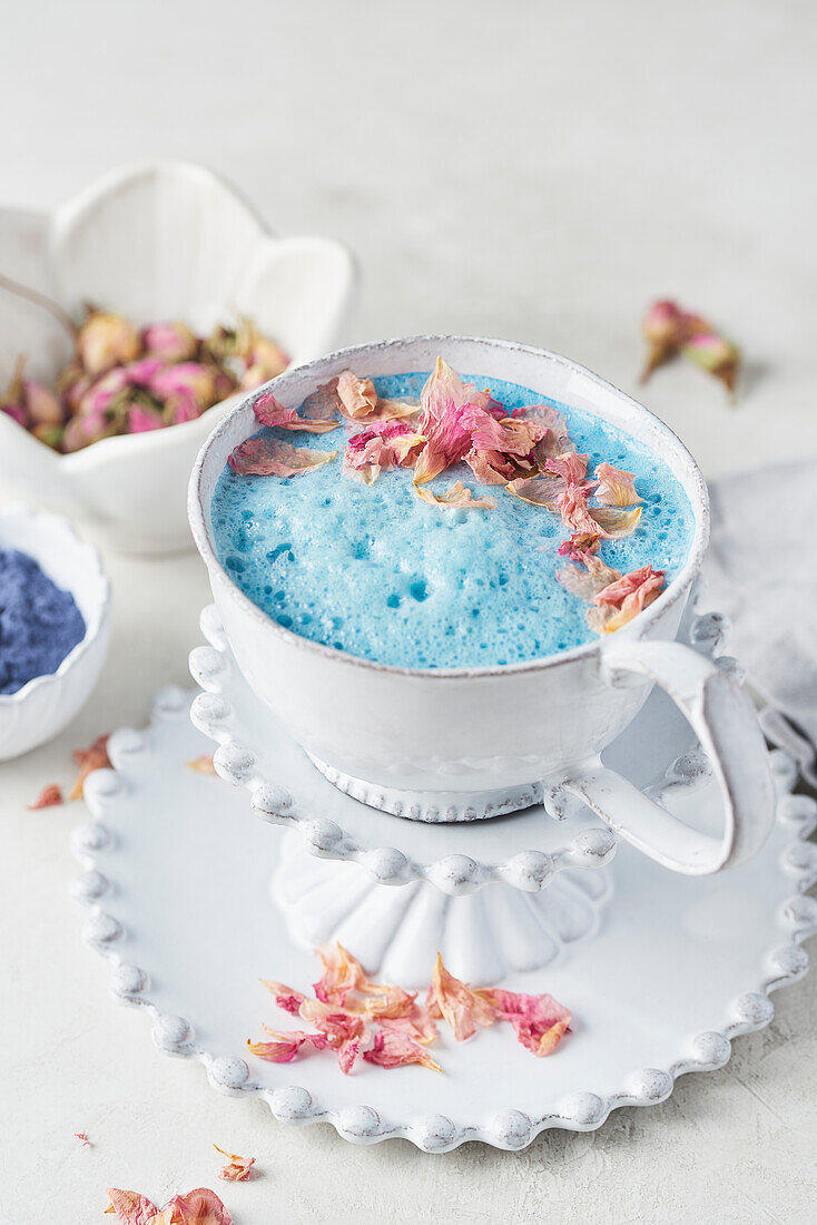 Teetasse mit veganem Schmetterlingsblütentee Latte mit getrockneten Rosenblättern
