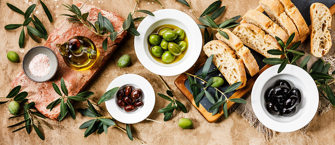 Italienisches Essen mit Oliven, Ciabatta-Scheiben und Olivenöl auf Travertin-Hintergrund Kopierfläche