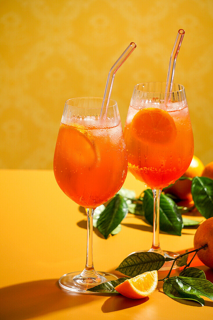 Aperol Spritz Cocktail mit Eis, ein beschlagenes erfrischendes Getränk, auf einem orangefarbenen Hintergrund, Sonnenlicht, Schatten, ein Sommergetränk in einem Weinglas