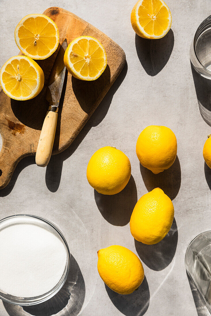 Lemons in hard light, surrounded with sugar, water and sliced lemons