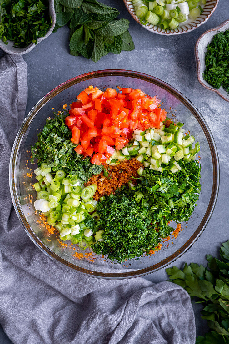Soaked bulgur wheat, chopped tomatoes, cucumber, mint, parsley and dill in a large glass bowl