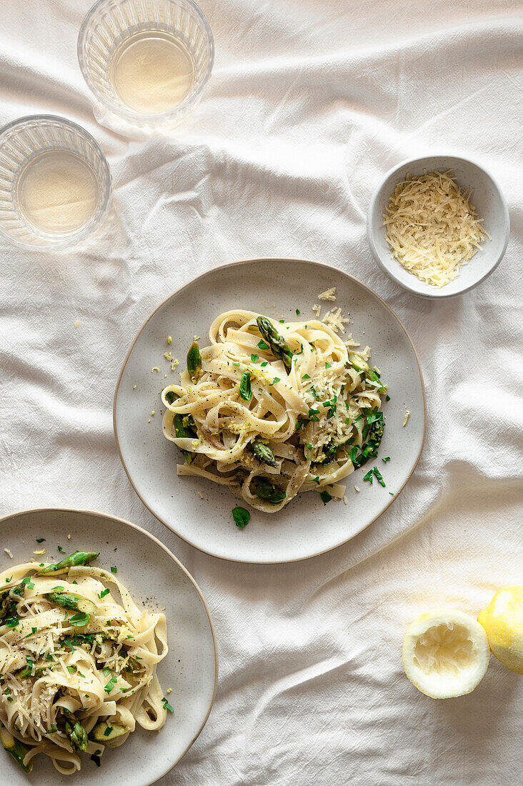 Zitronige Pasta mit Spargel, veganem Käse und frischem Basilikum auf einem frühlingshaften, luftigen Tisch