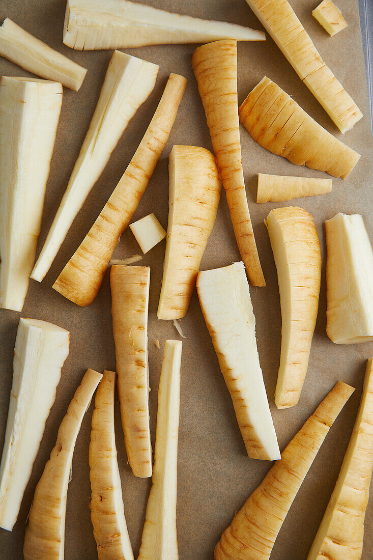 Top view of uncooked sticks of raw parsnip placed on parchment paper before preparation during cooking process