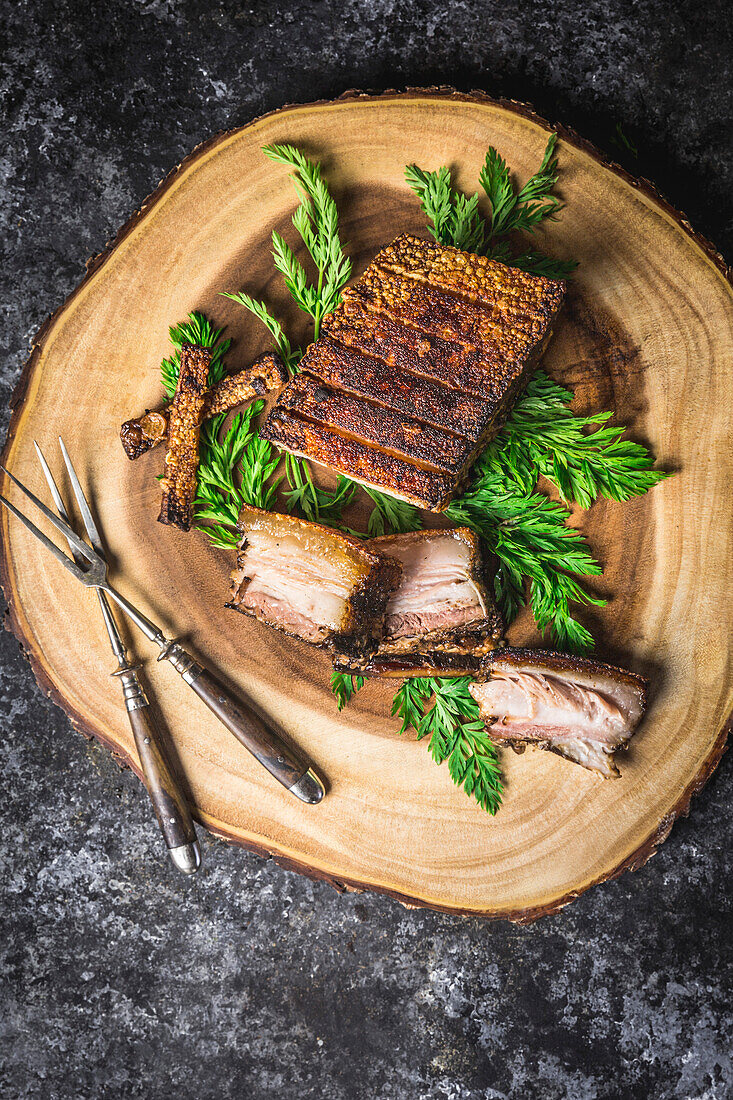 Sliced crispy pork belly on a wooden plate with forks and green garnish