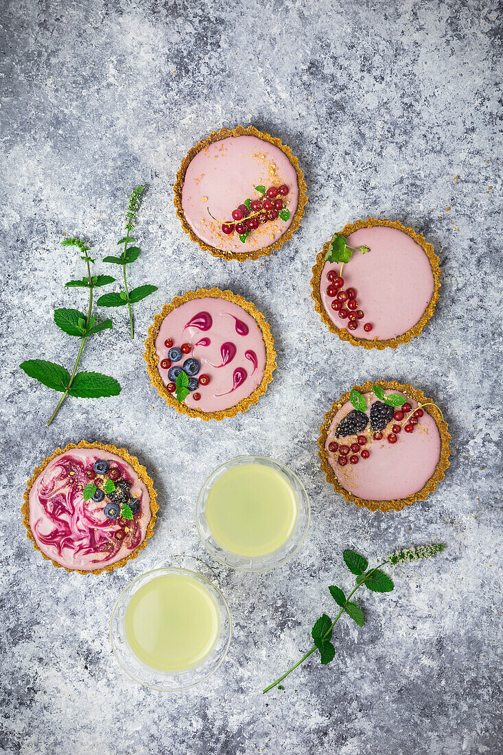 Arrangement of four small tarts filled with berry cream, decorated with fresh fruit and mint, and 2 glasses of limoncello