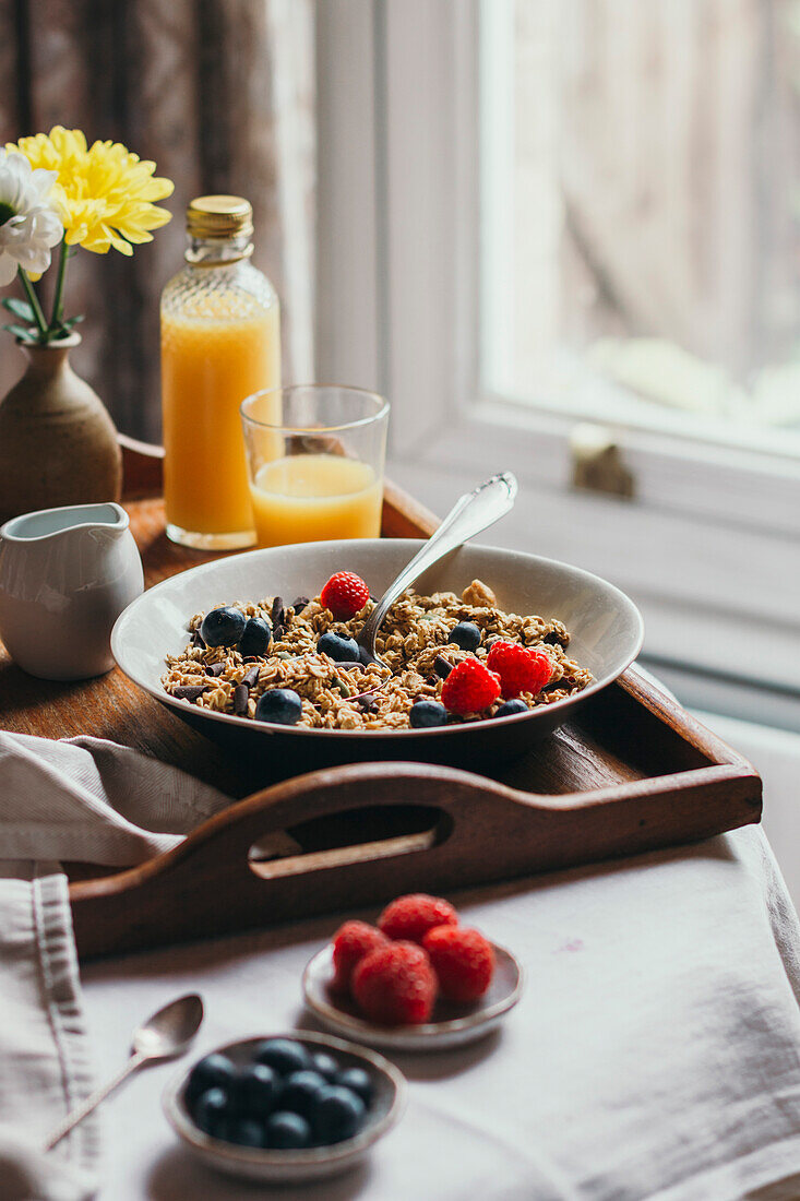 Breakfast tray with muesli, berries and juice next to a window