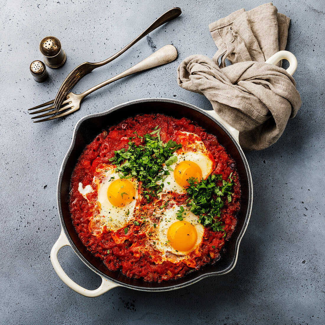 Breakfast shakshuka fried eggs with tomatoes in a pan against a concrete background