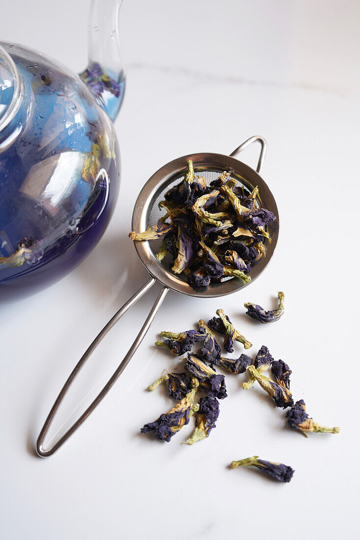 Blue butterfly pea flower tea on a white marble background. Tea strainer with dried flowers close-up