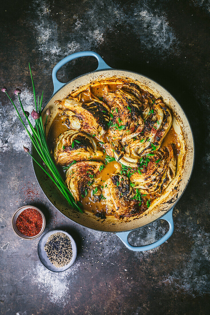 Braised cabbage wedges in a casserole with sauce and chive flower garnish 1