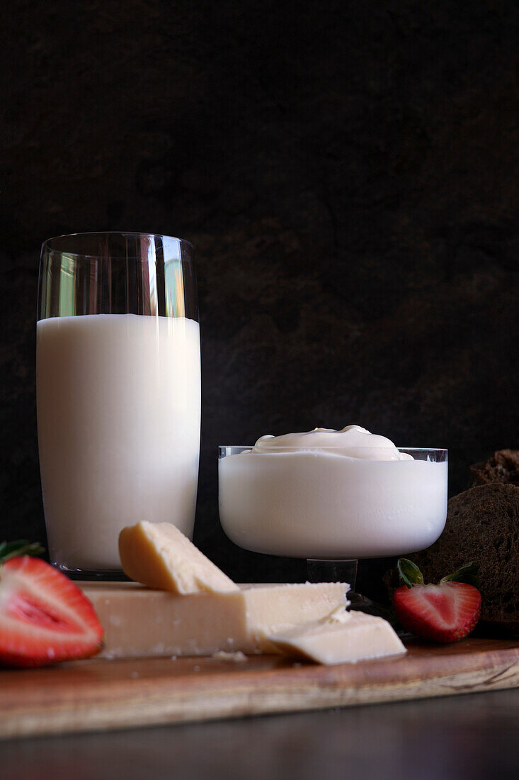 Healthy probiotic dairy, including kefir, Greek style yoghurt, and parmgiano reggiano cheese against a dark background.