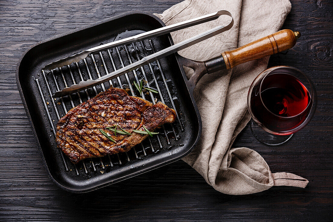 Grilled Steak Striploin in grill iron pan and red wine on black burned wooden background